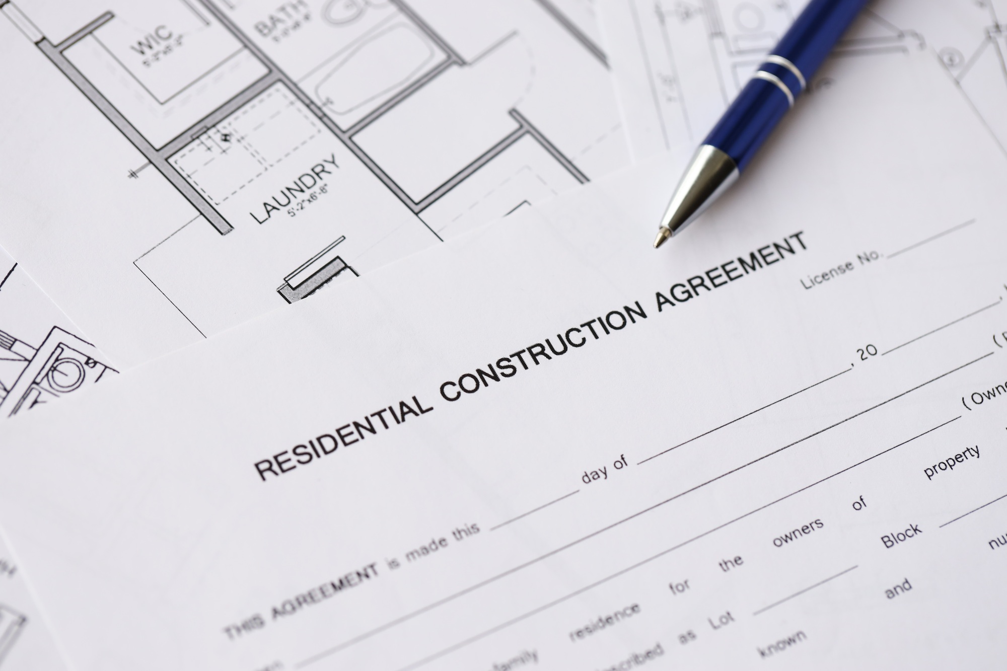 Pen on residential construction agreement and planning blueprints of residential building project